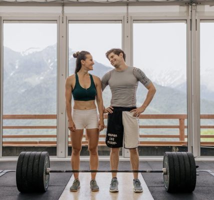 A couple in activewear standing together in a gym with weightlifting equipment.
