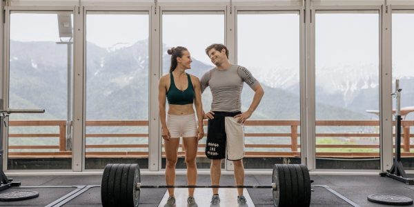 A couple in activewear standing together in a gym with weightlifting equipment.